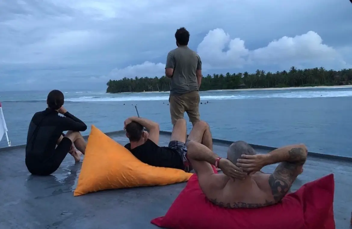Guests on beanbags at dusk watching surfers on a reef break