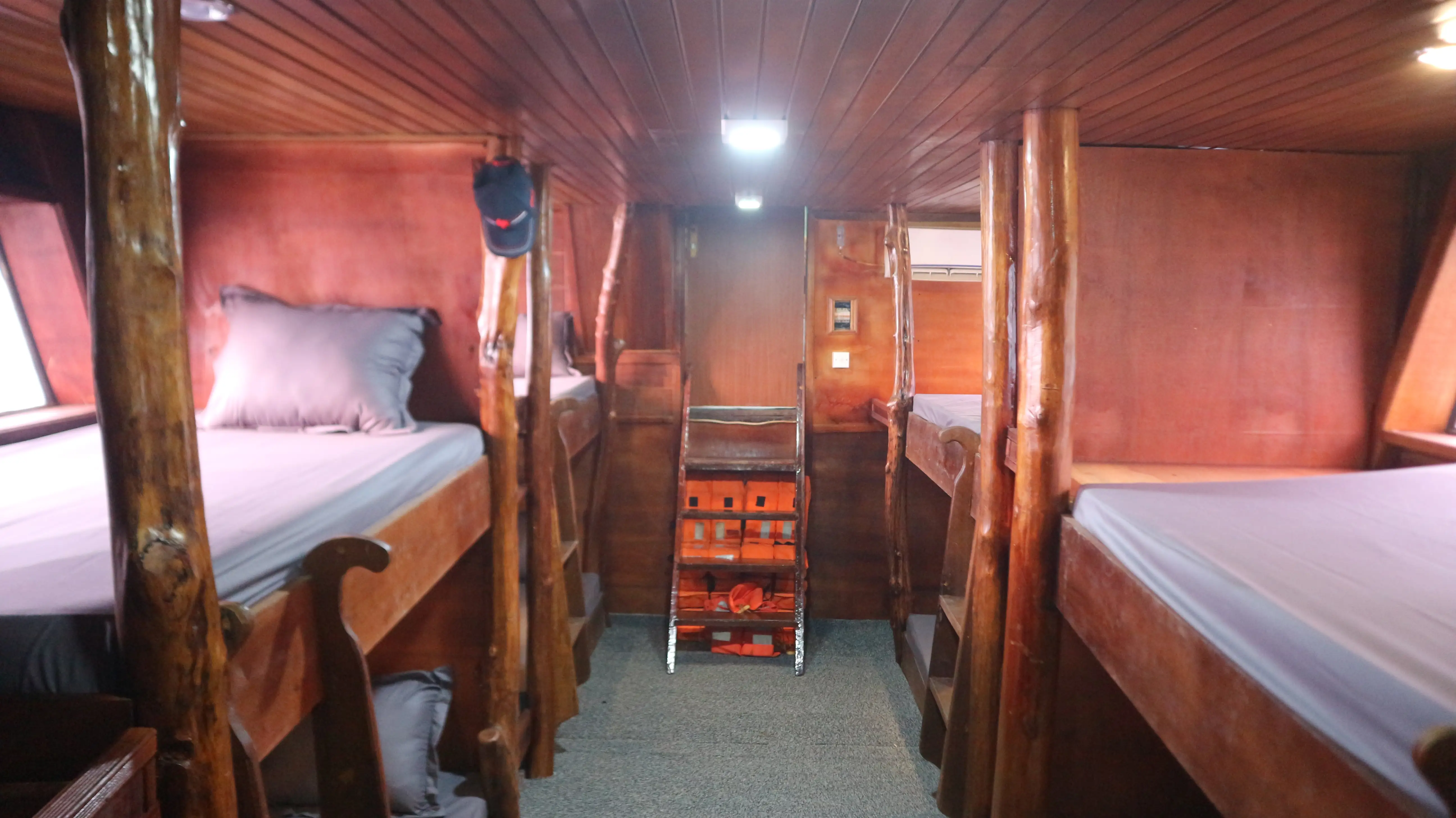 Timber-panelled cabin below deck with made-up bunk beds either side of a central ladder