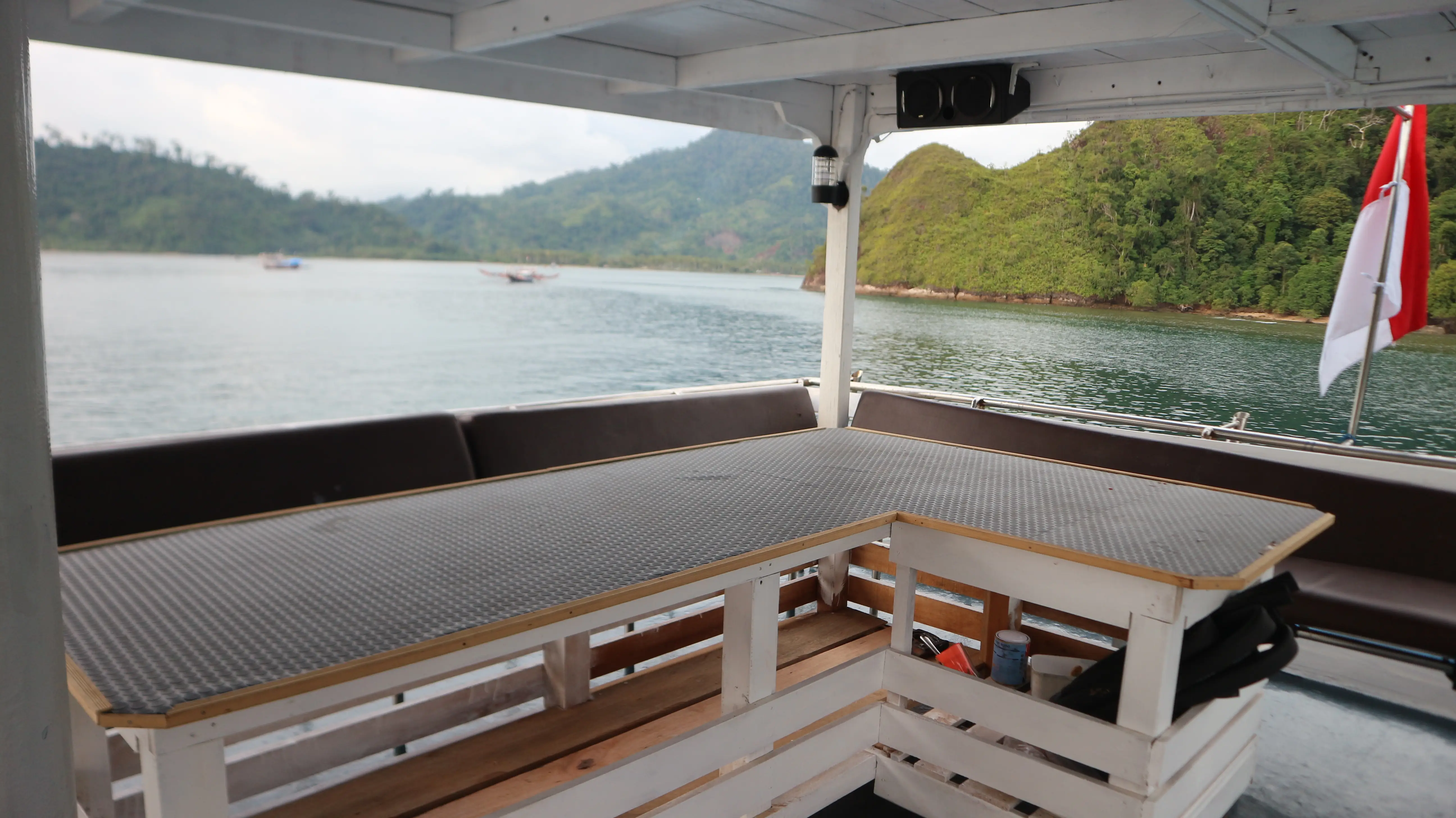 Covered aft deck with an L-shaped table and bench seating overlooking a forested bay