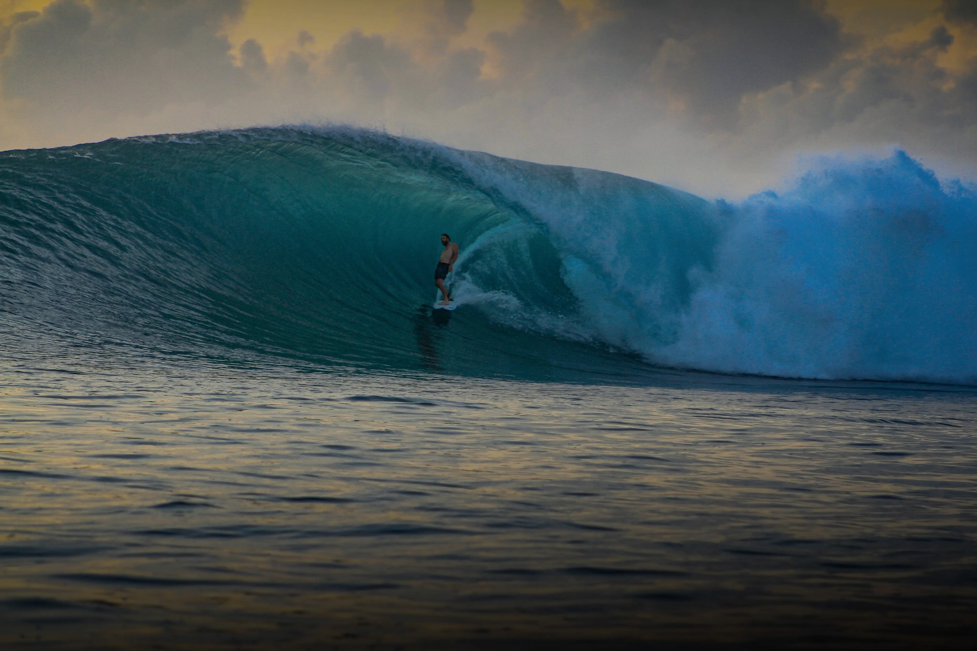 Surfer deep inside a large glassy barrel at dusk under golden clouds