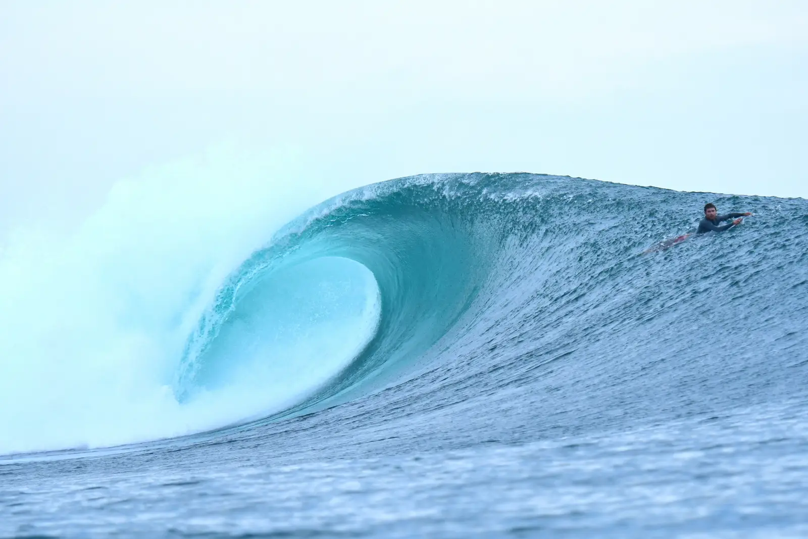 Empty turquoise barrel peeling left with a bodyboarder paddling over the shoulder