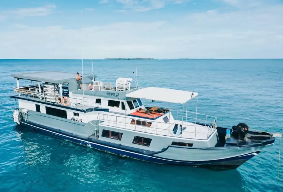 The boat's bow and covered foredeck over clear turquoise shallows