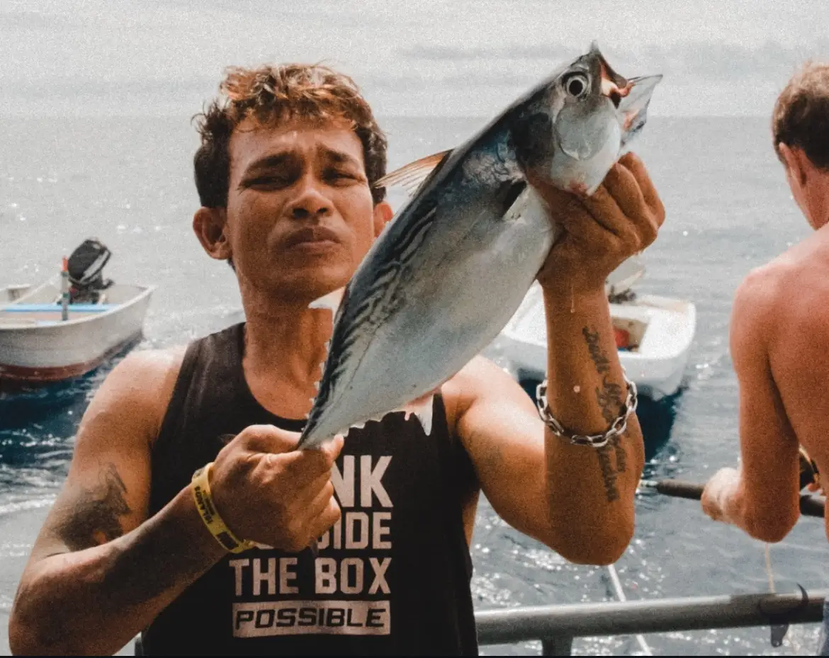 Crew member holding up a freshly caught skipjack tuna at the boat rail