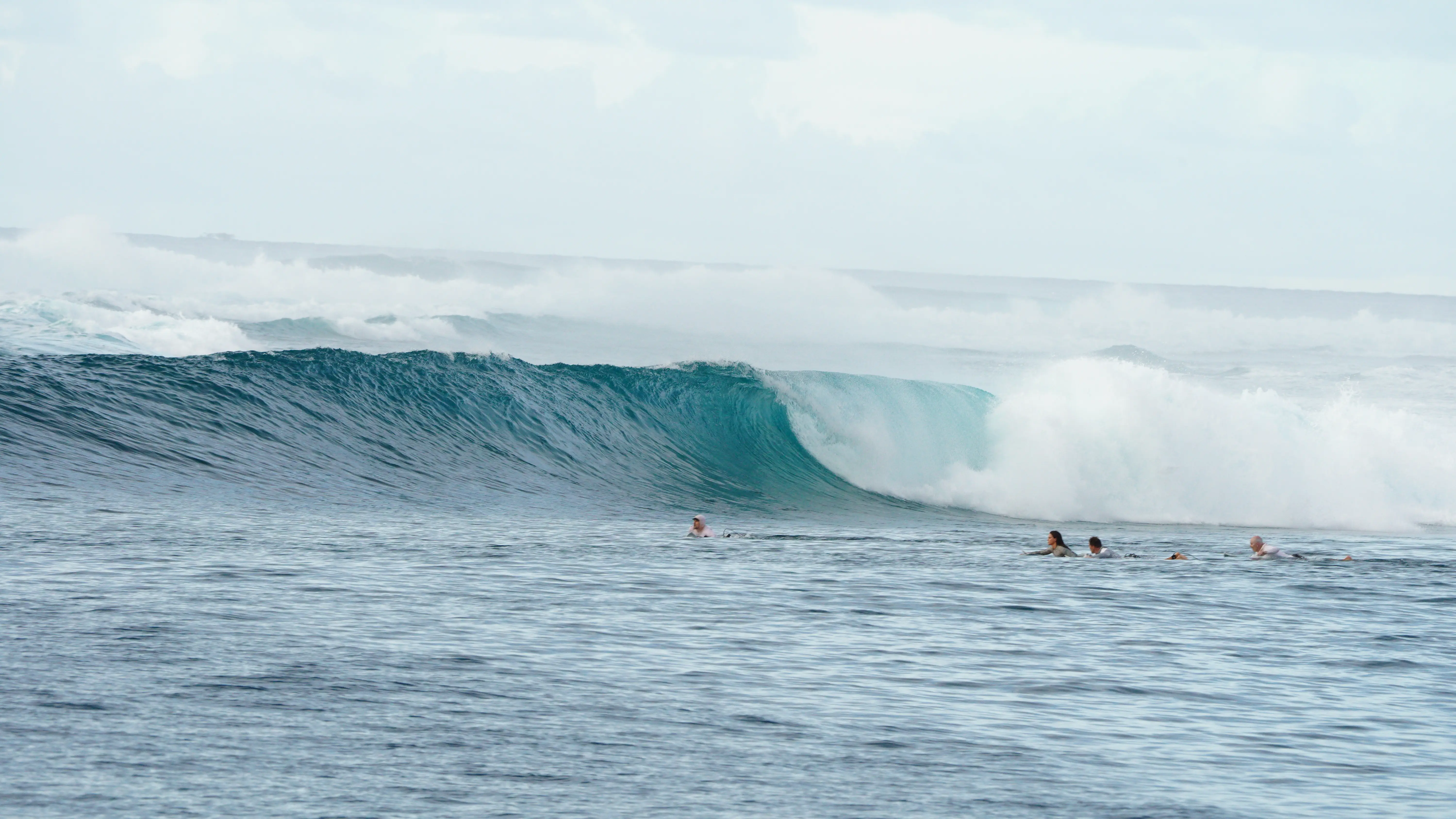 Glassy turquoise wave peeling toward surfers waiting in the line-up