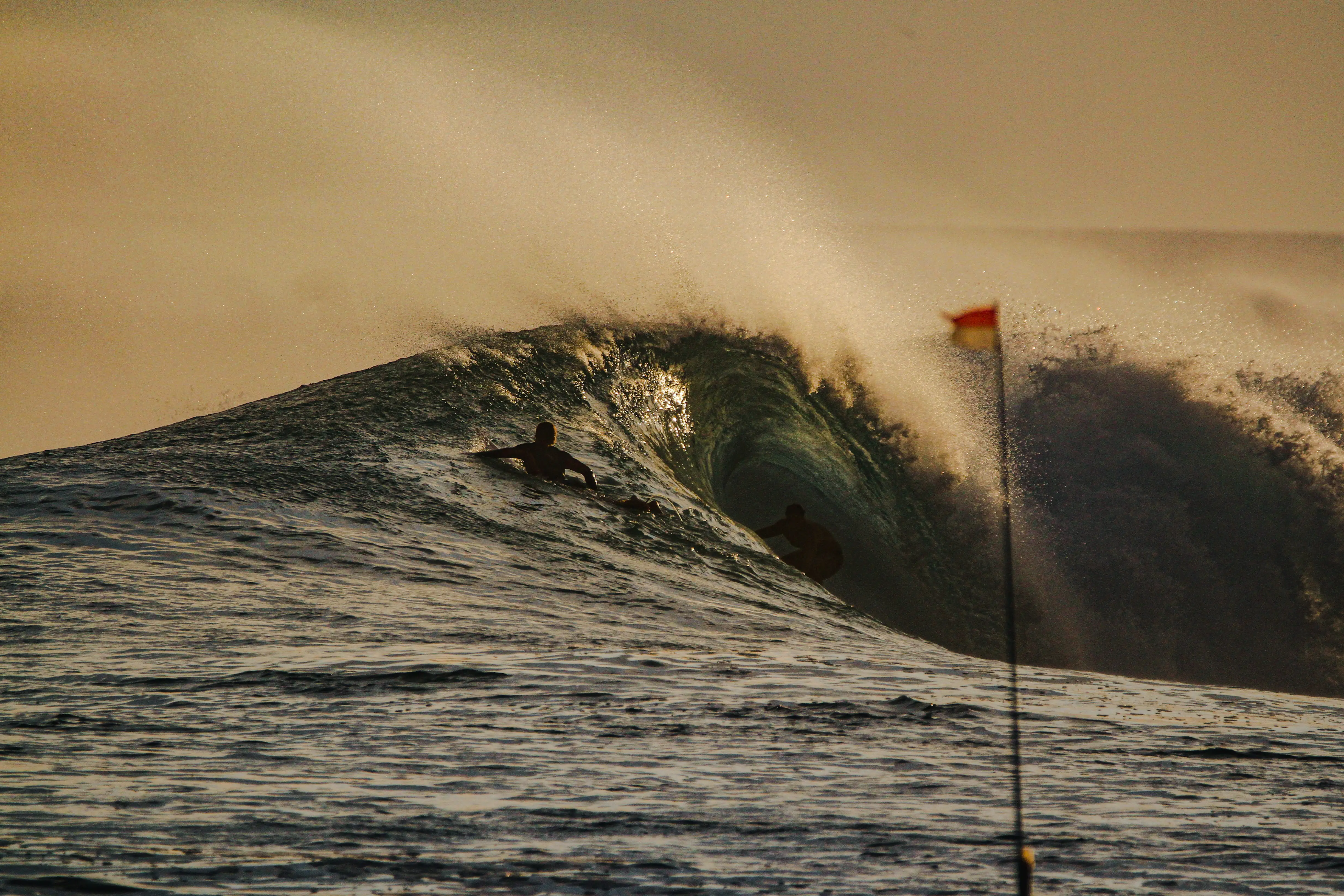 Silhouetted surfer inside a golden backlit barrel at sunset