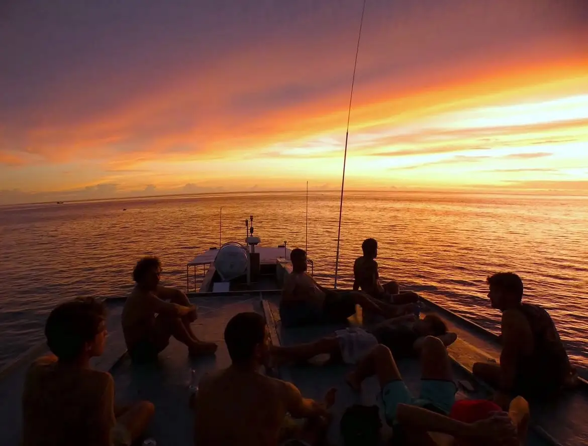 Guests on the bow deck watching an orange and purple sunset