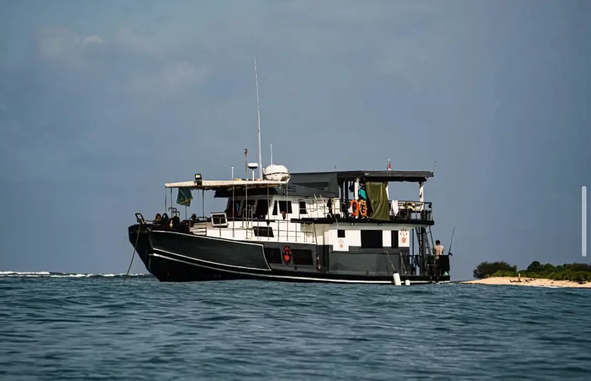 The dark-hulled boat anchored off a sandy island shoreline