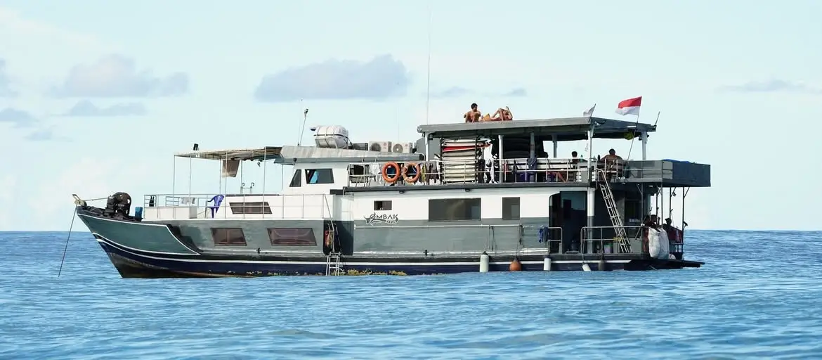 The boat at anchor with guests on deck and the Indonesian flag flying