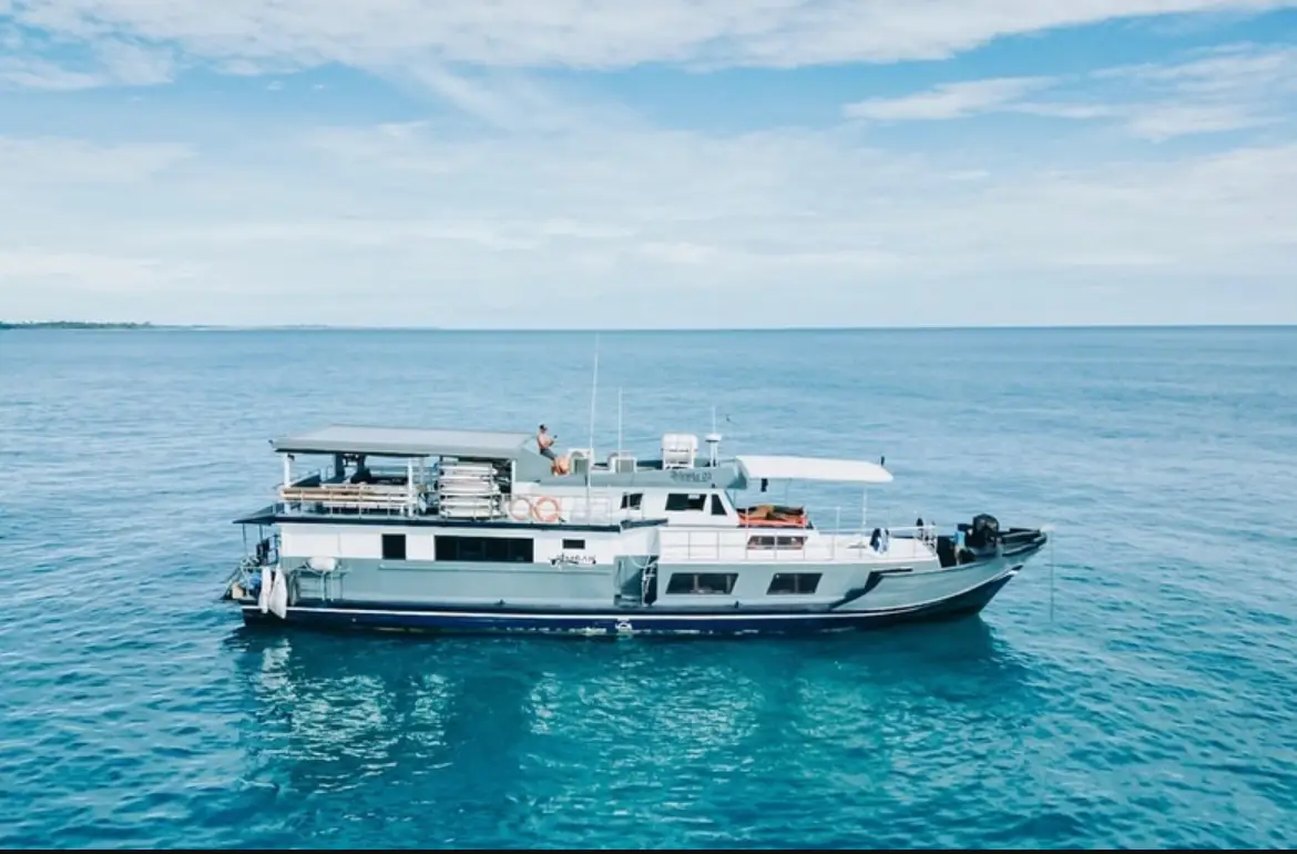 Full side profile of the Ombak Kabau at anchor on flat turquoise water