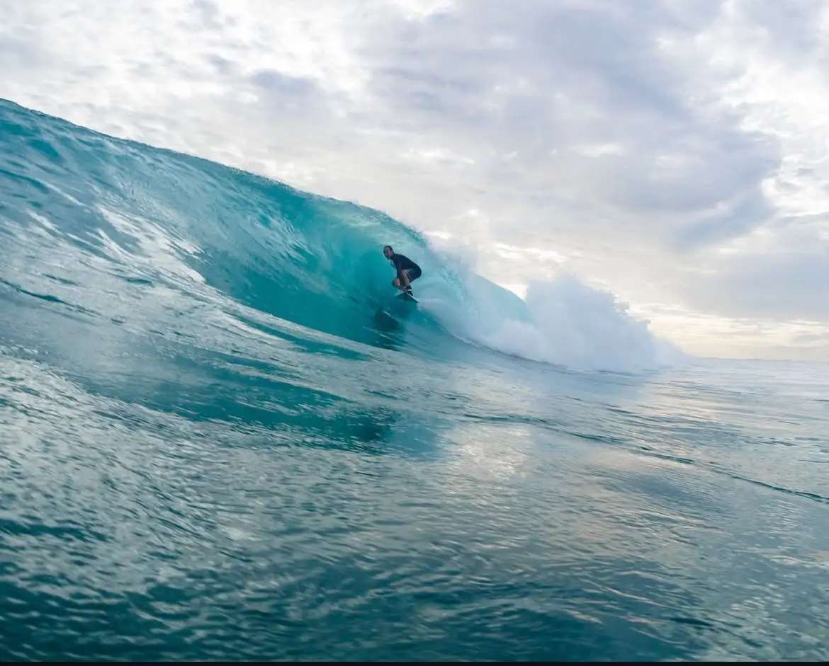 Surfer tucked into a wide silvery-blue barrel, shot from the water