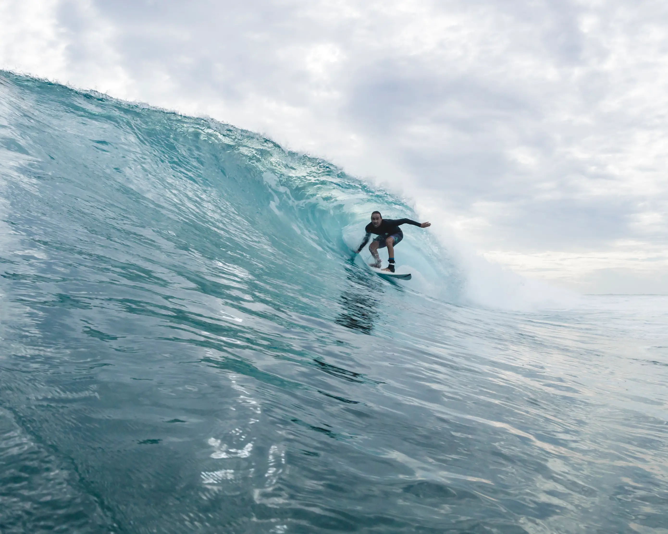 Surfer riding out of a silvery barrel under an overcast sky