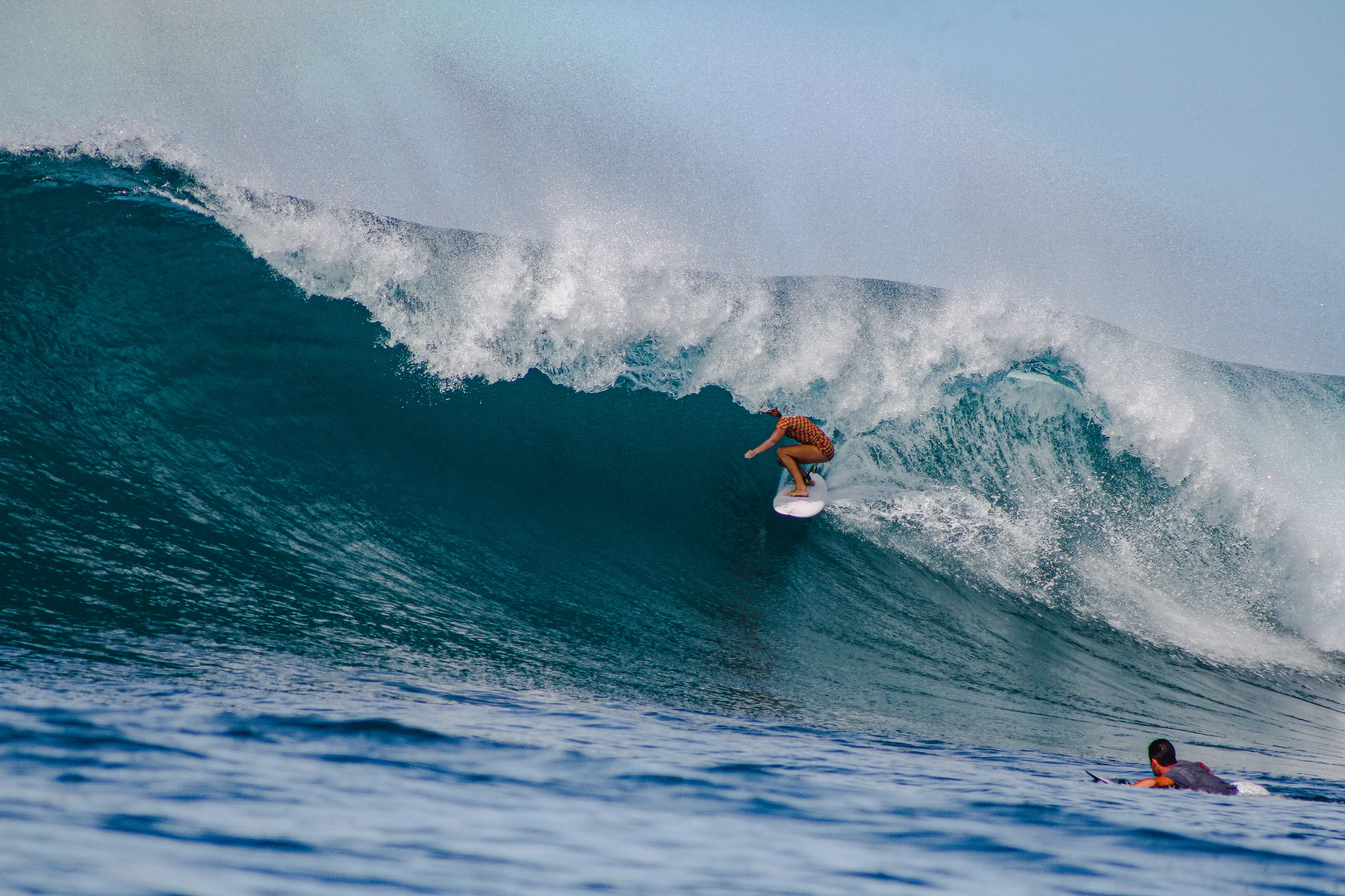 Surfer dropping down the face of a large heaving teal wave