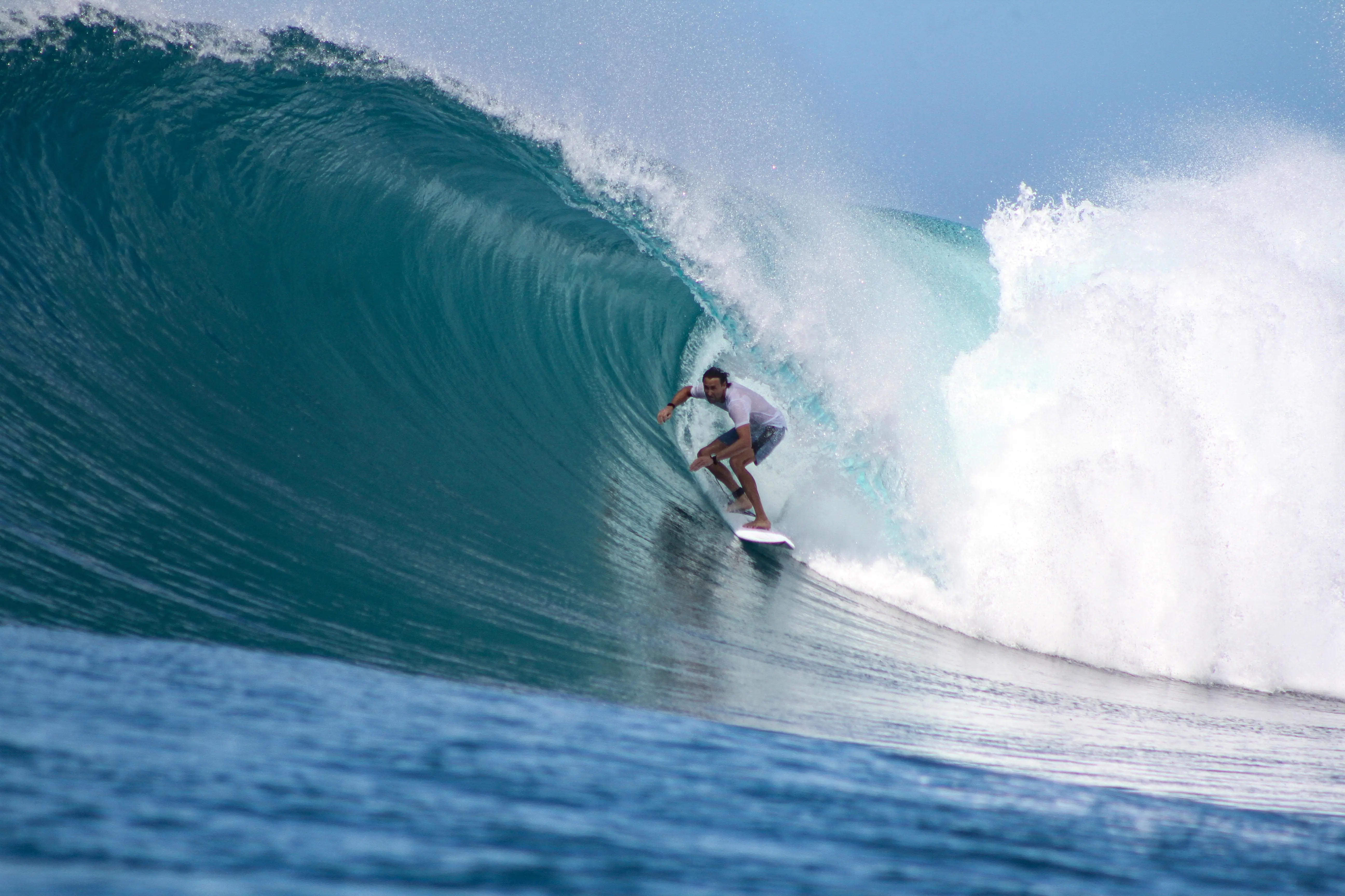 Surfer in a white shirt riding inside a glassy turquoise barrel